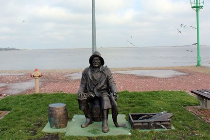 zeigt Fischerfigur aus Bronze, mit Fischkiste