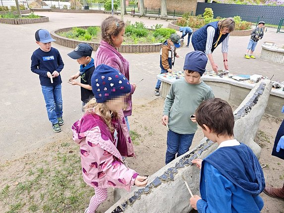 zeigt Kinder beim Aufkleben von schwarzen Tonscherben auf Betonechse