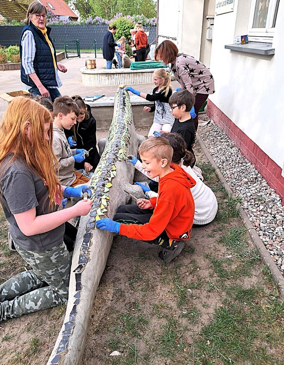 zeigt Kinder beim Aufkleben von Tonscherben auf einer Betonechse