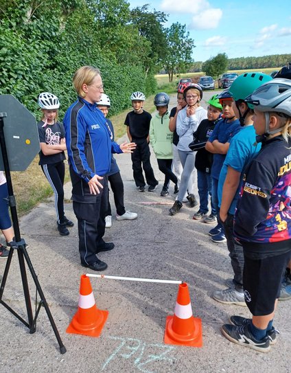 zeigt Kindergruppe und Polizistin bei Erklärung