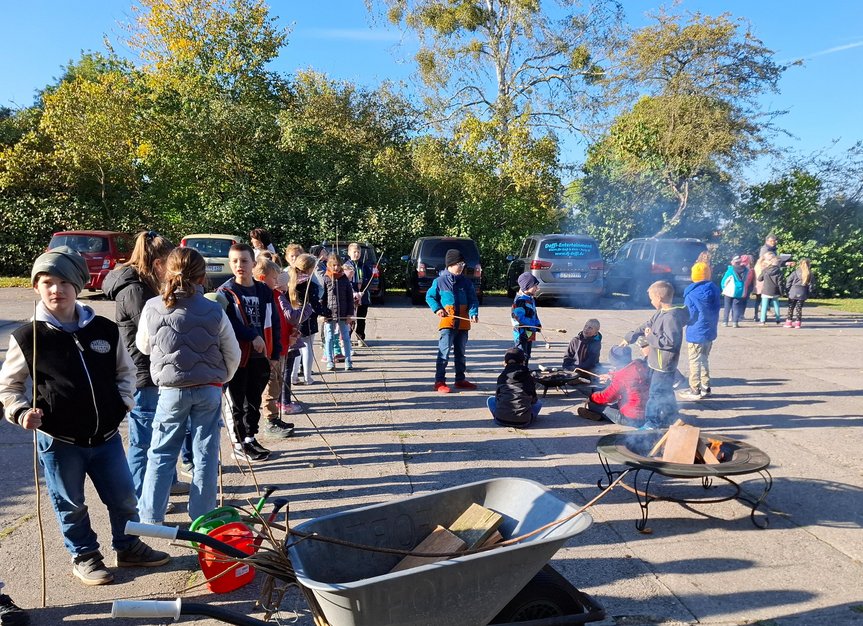 zeigt Schüler auf dem Schulhof beim Stockbrot backen