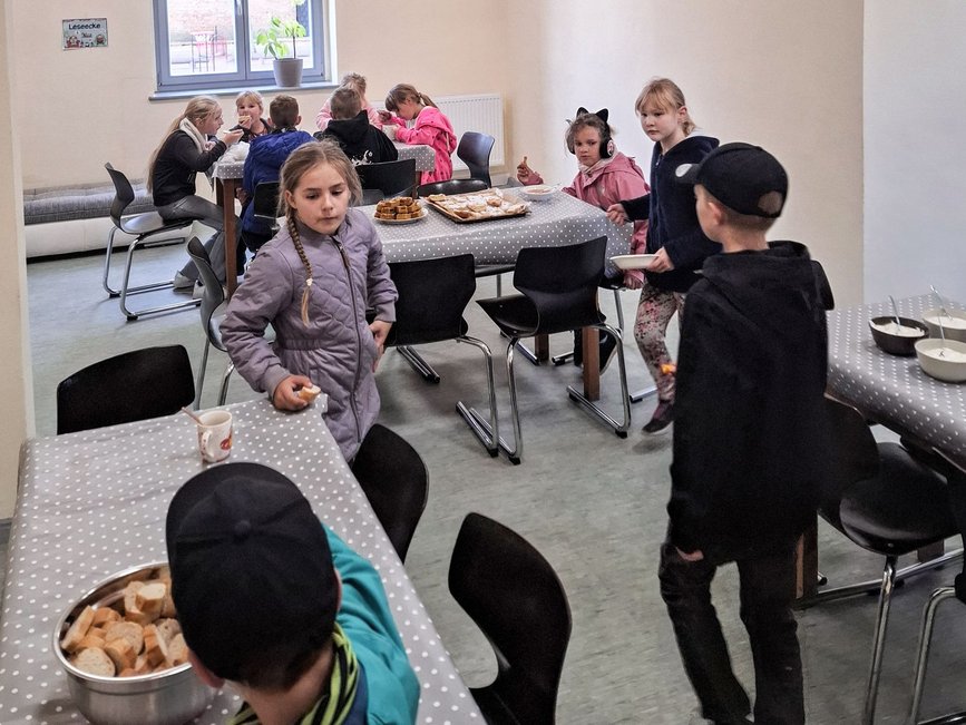 zeigt Raum mit essenden Kindern und verschiedenen Gerichten auf den Tischen