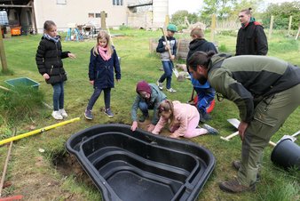 zeigt Kinder beim Absenken des Fertigteiches