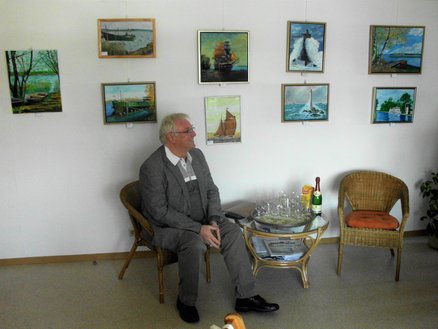 Lesestübchen zeigt Ausschnitt einer Bilderausstellung mit einem sitzenden Mann davor